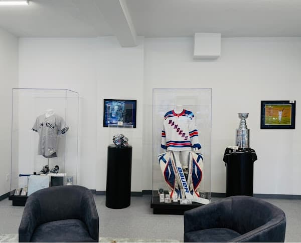 Sports memorabilia display featuring a Yankees jersey, Rangers goalie equipment, and a silver trophy.