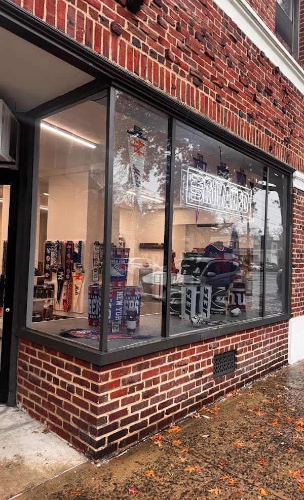 A brick storefront window displays New York sports team merchandise, including pennants and mugs.